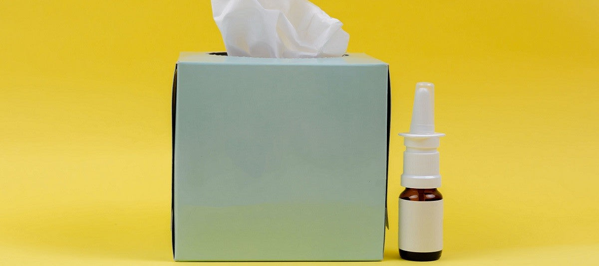 Box of tissues and bottle of nasal spray against yellow background