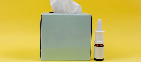 Box of tissues and bottle of nasal spray against yellow background