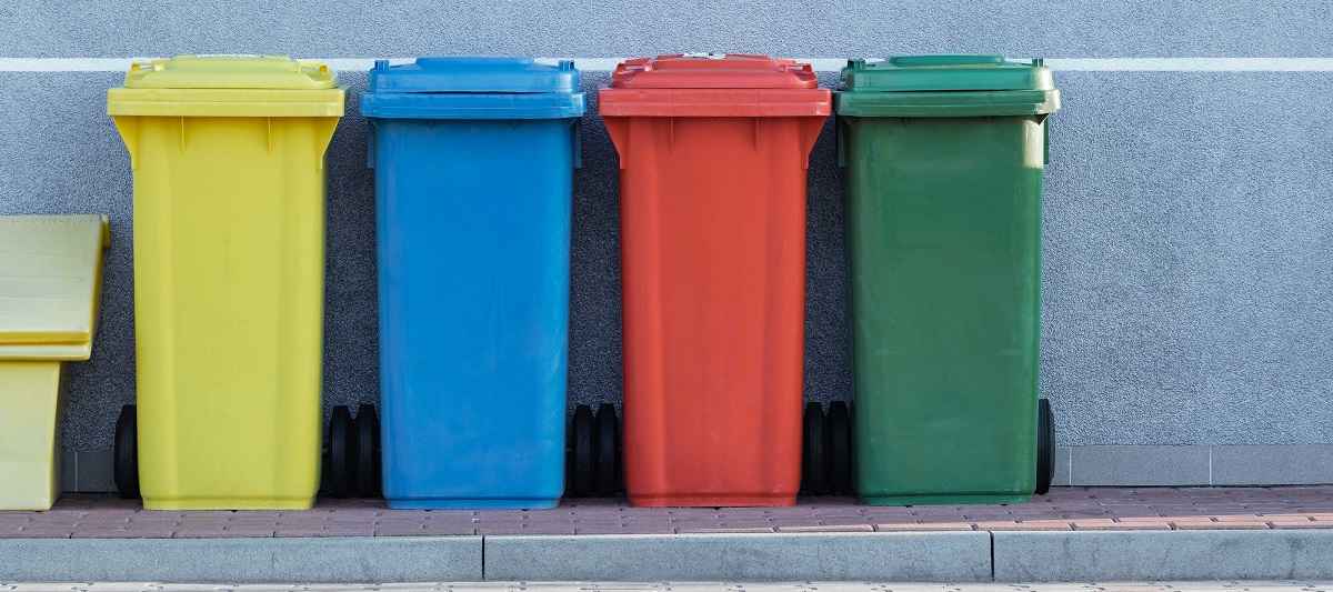 Green, red, blue, and yellow trash bins lined up against building