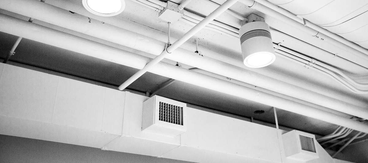 White and grey industrial ceiling with large lights, ducts, and air vents